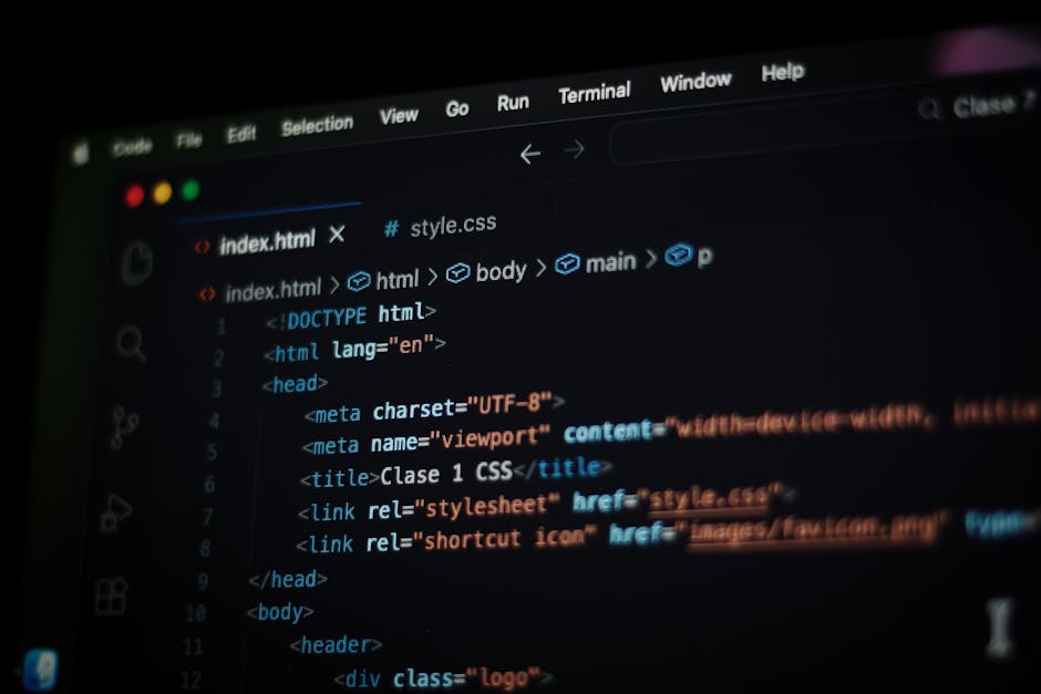 A close-up view of a person's hand typing on a silver laptop keyboard placed on a wooden desk. The laptop screen displays lines of code or programming text with a dark background and multicolored synt